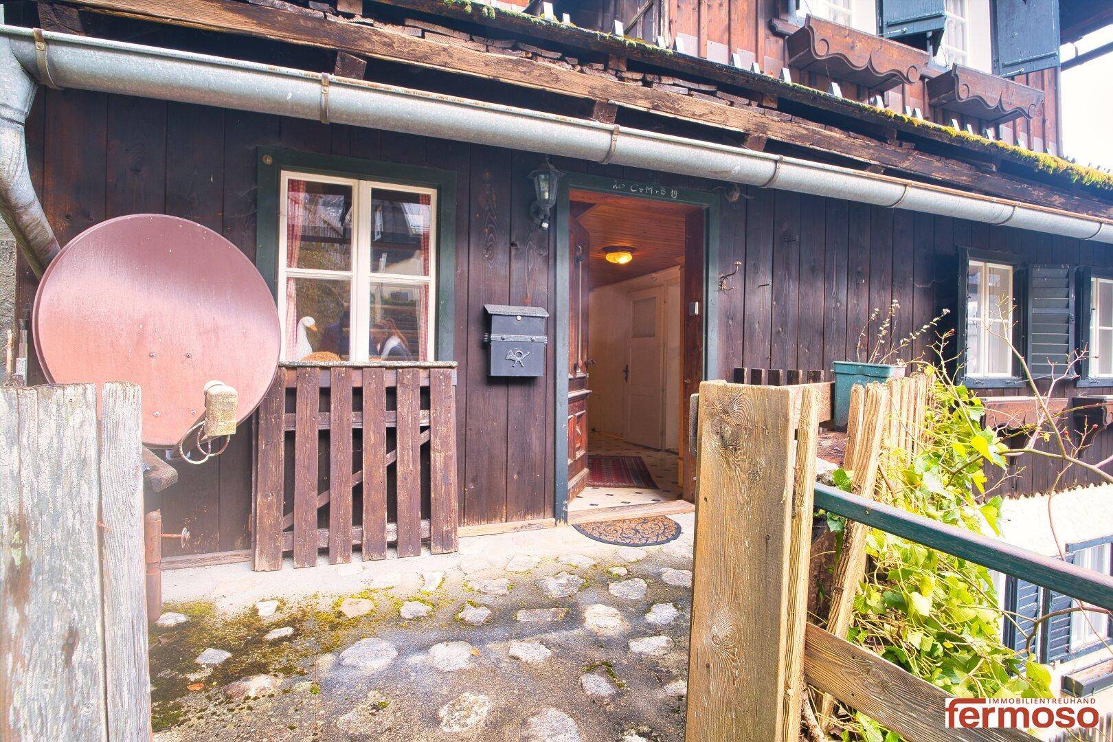Eingangsbereich eines traditionellen Holzhauses mit Satellitenschüssel und rustikalem Steinweg.