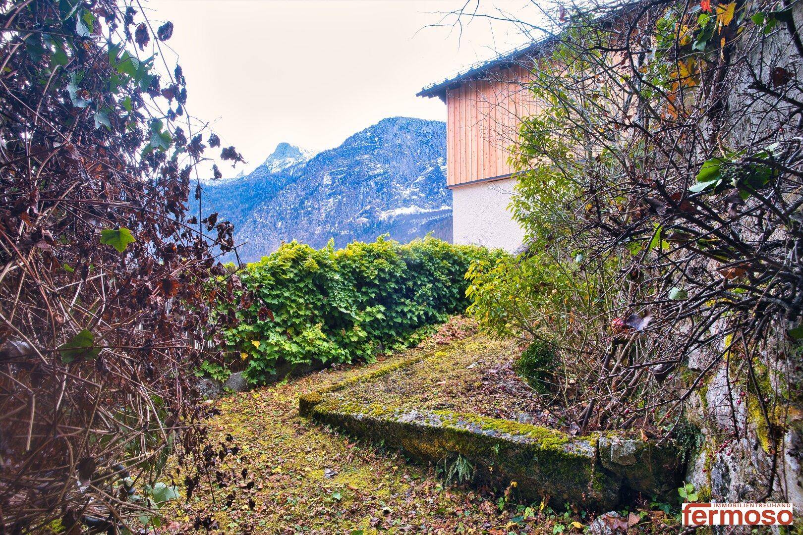 Verwunschener Gartenweg mit einer dichten Hecke und majestätischen Bergen im Hintergrund.