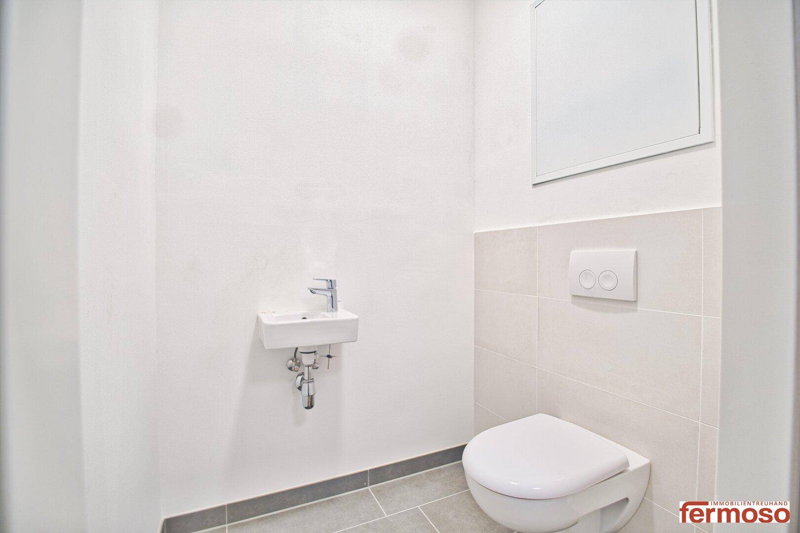 Separates WC mit wandhängender Toilette und kleinem Handwaschbecken.