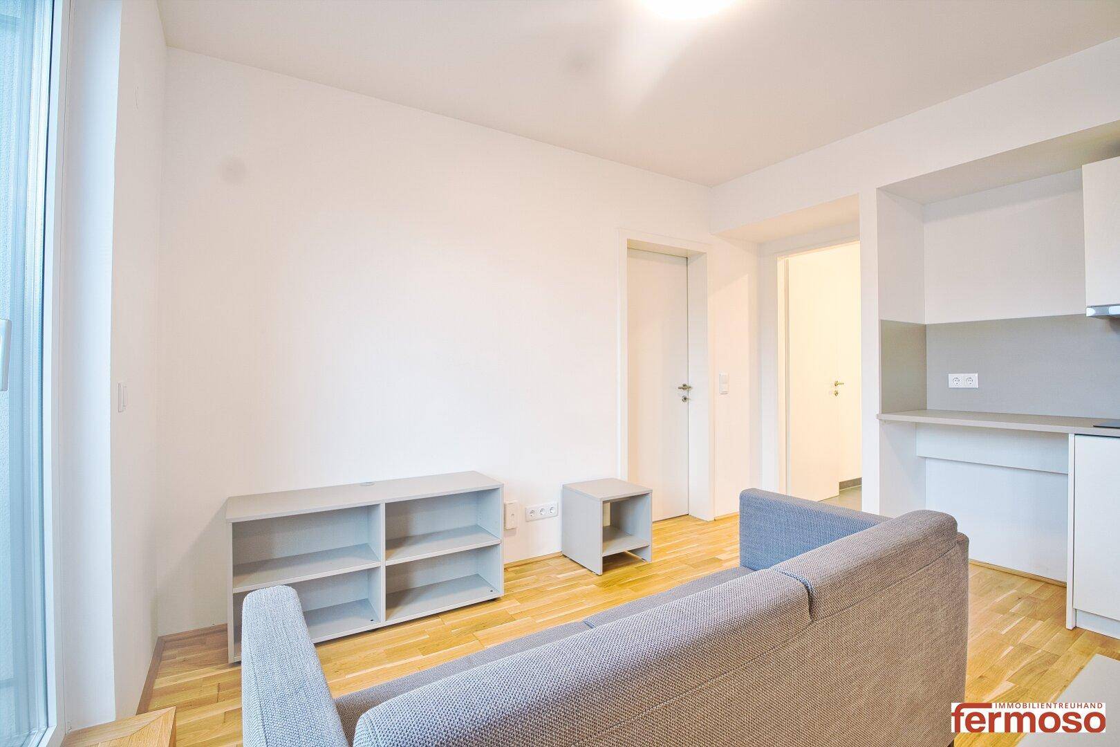 Gemütlicher Wohnbereich mit grauem Sofa, niedrigen Regalen und hellem Holzparkett.