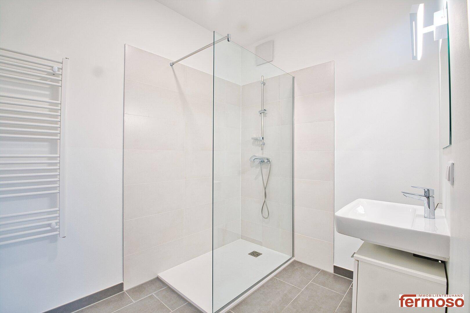 Modernes Badezimmer mit ebenerdiger Dusche, Einzelwaschbecken und beheiztem Handtuchhalter.