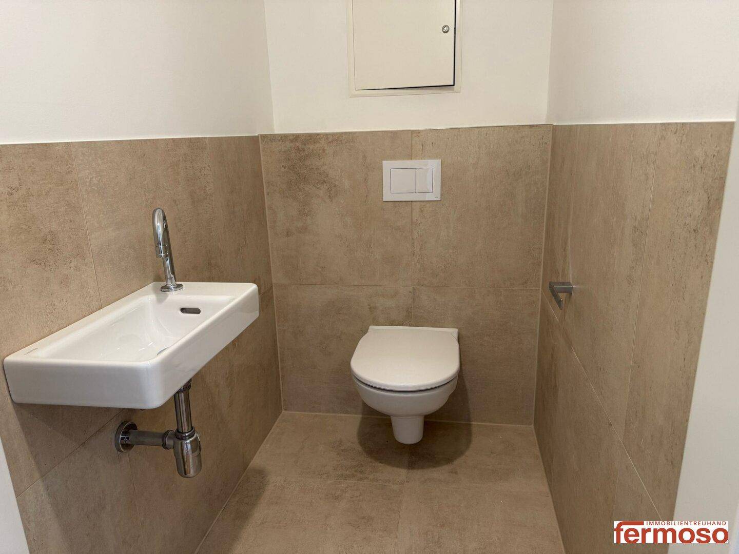 Gäste-WC mit beigefarbenen Fliesen, wandhängendem WC und kleinem Handwaschbecken.