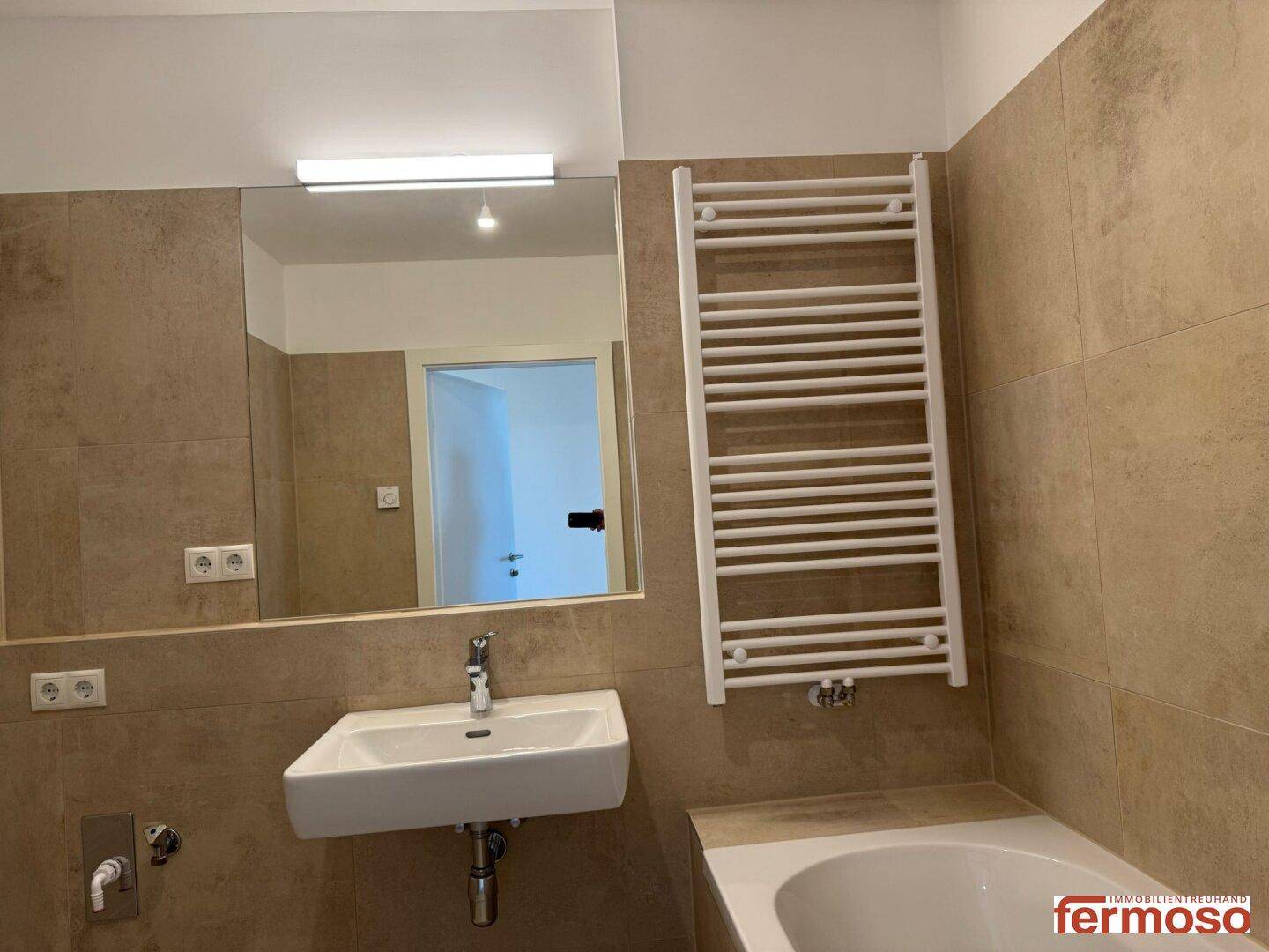 Modernes Badezimmer mit beigefarbenen Fliesen, Badewanne, Waschbecken und beheiztem Handtuchhalter.