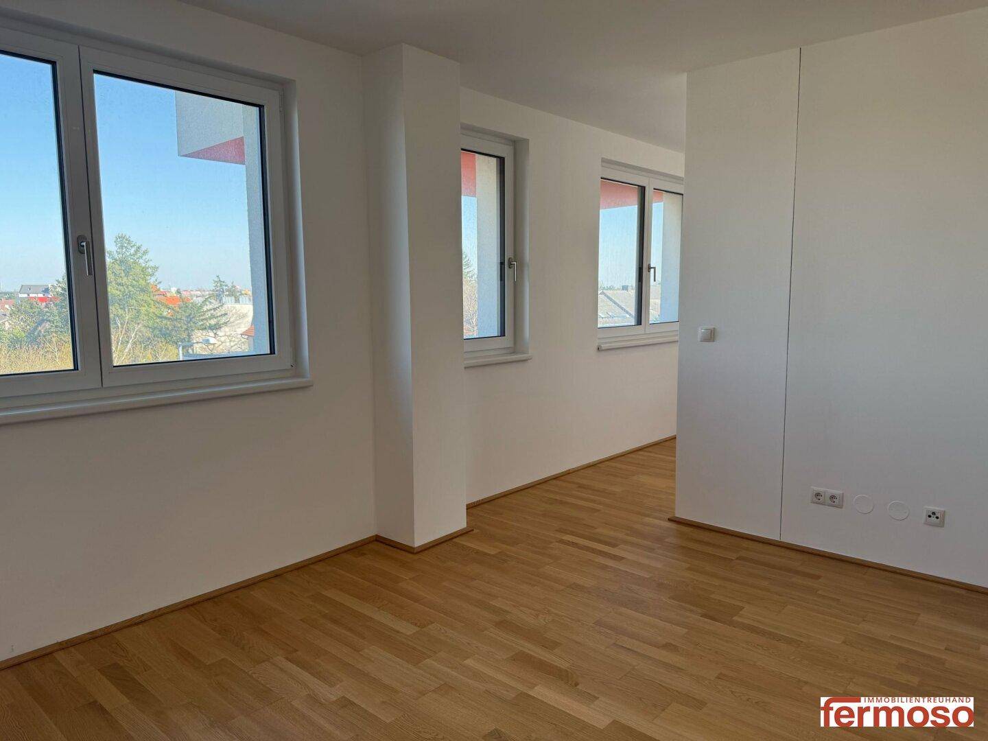 Heller Raum mit Parkettboden und mehreren Fenstern, die viel Tageslicht hereinlassen.