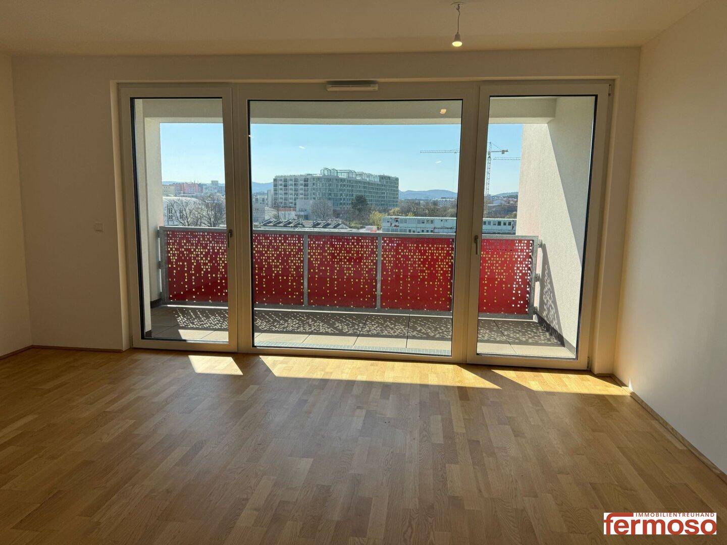 Helles Wohnzimmer mit Parkettboden und großem Schiebefenster zum Balkon.