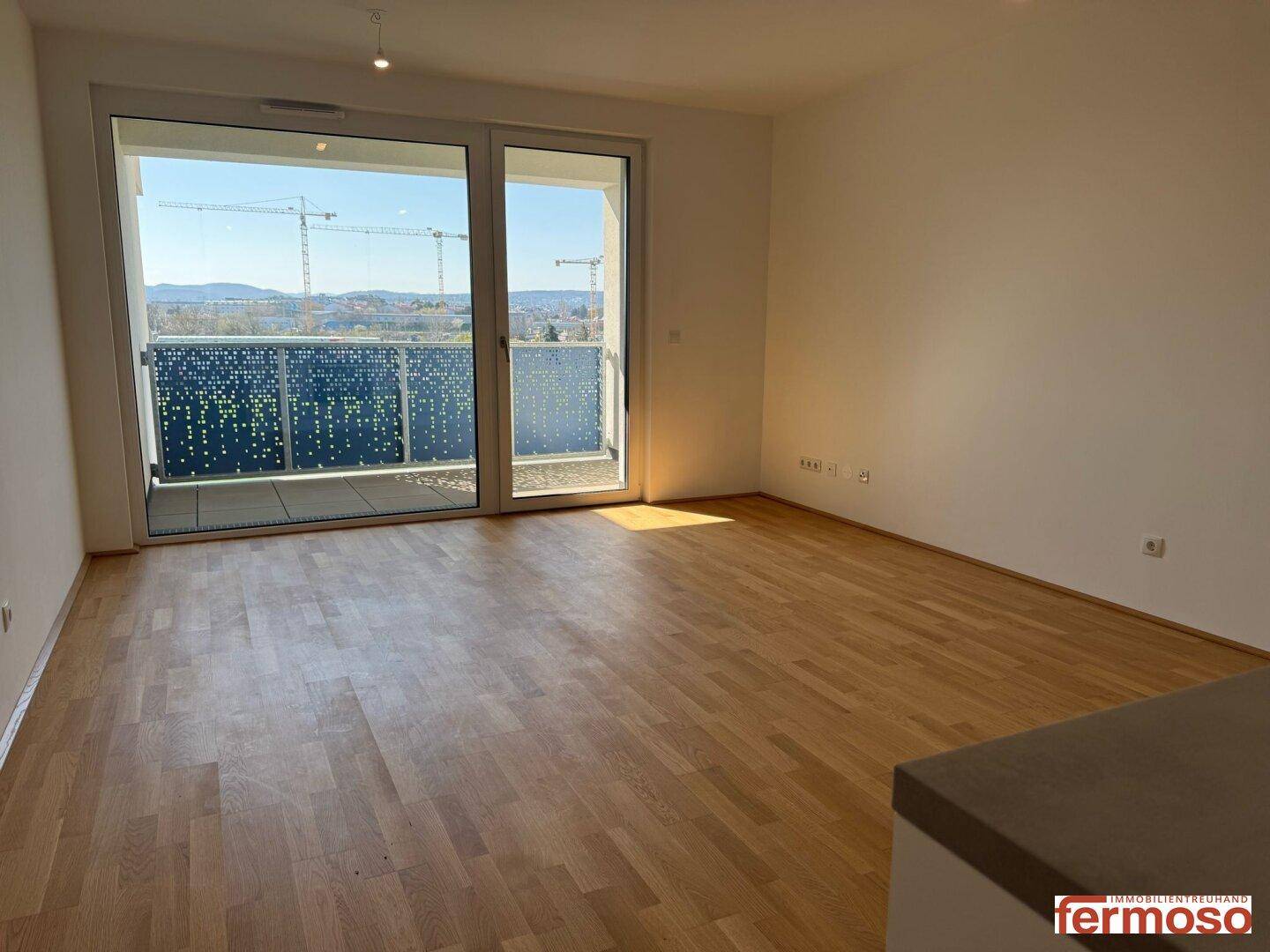 Lichtdurchfluteter Wohnbereich mit Holzboden und Zugang zu einem Balkon mit Weitblick.