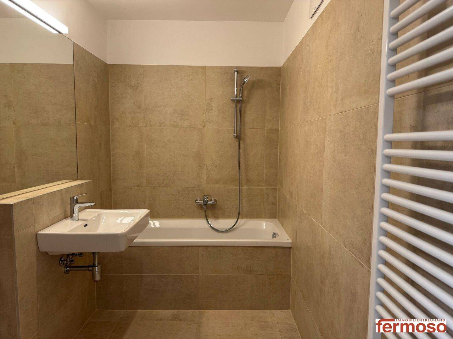 Badezimmer mit Badewanne, Waschbecken und beheiztem Handtuchhalter.