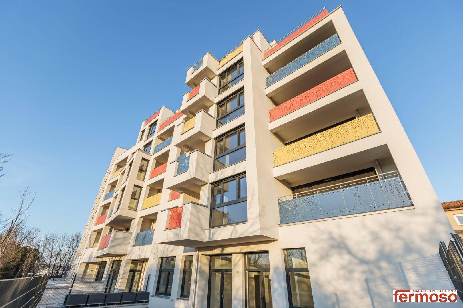 Neubau mit moderner Architektur, farbigen Balkonbrüstungen und vielen Fenstern.