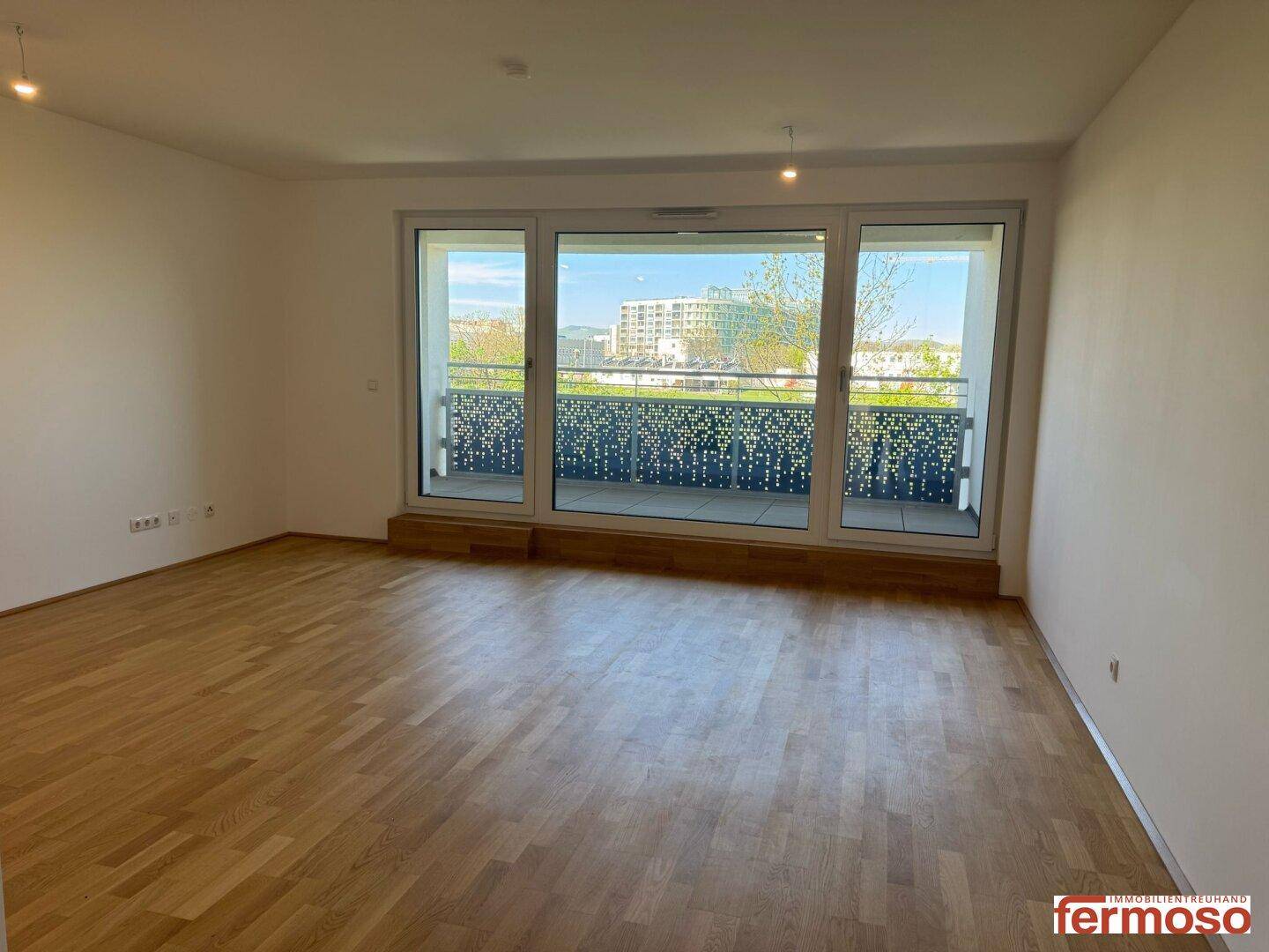 Geräumiges Wohnzimmer mit Parkettboden und Zugang zu einem Balkon, bietet viel Tageslicht.