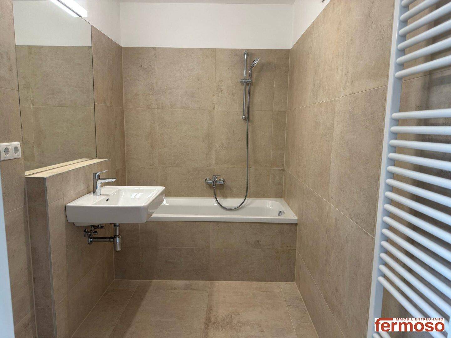 Modernes Badezimmer mit beigefarbenen Fliesen, Badewanne und beheiztem Handtuchhalter.