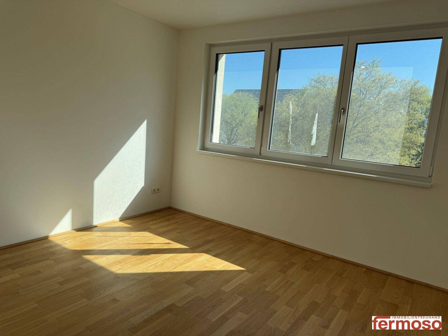 Schlafzimmer mit Parkettboden und großen Fenstern, die viel Sonnenlicht hereinlassen.