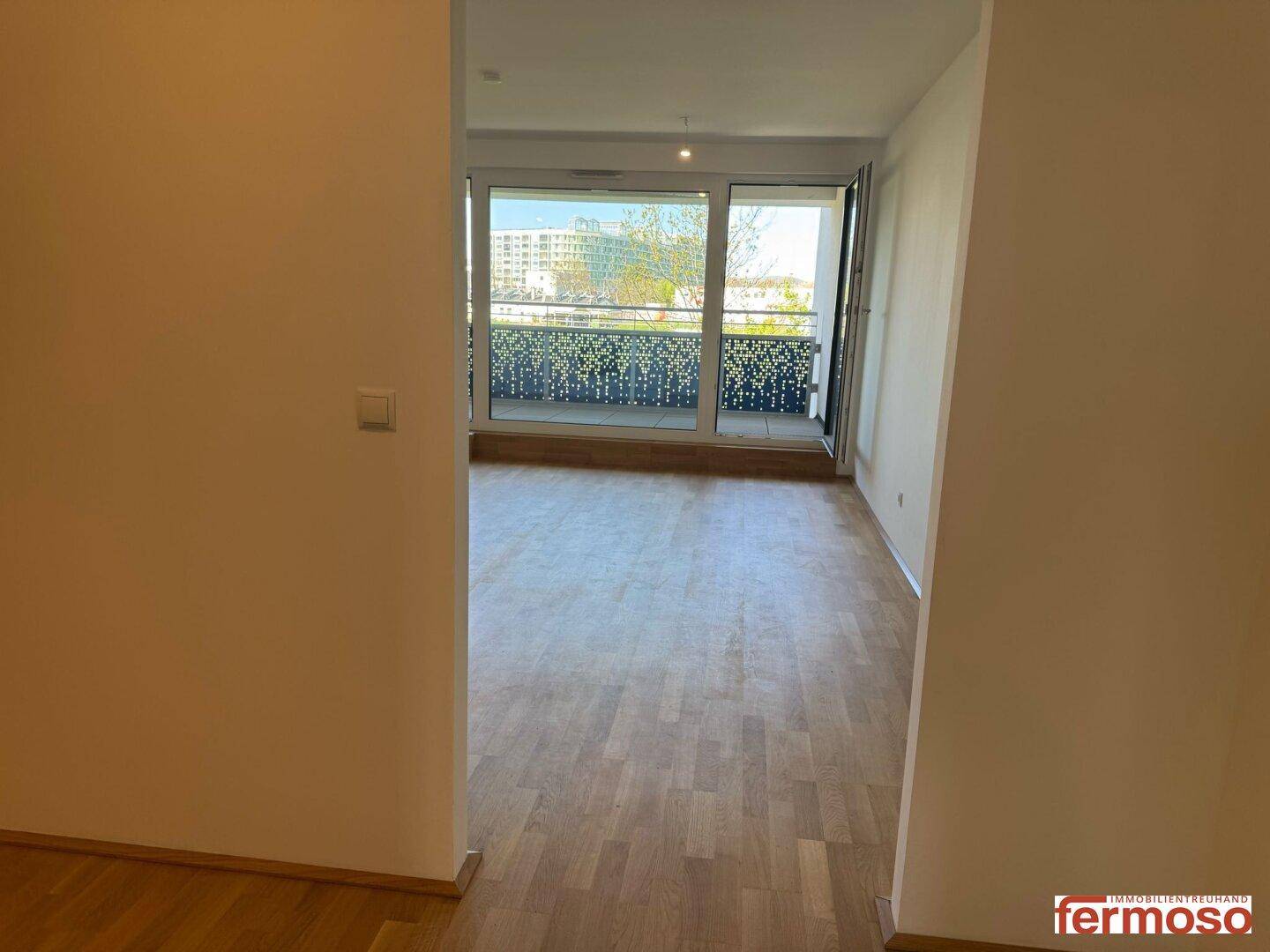 Heller Flur mit Parkettboden, der zum Wohnbereich mit Balkonzugang führt.