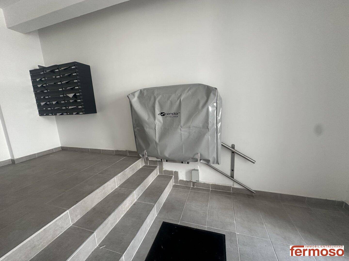 Eingangsbereich mit Treppe, Briefkästen und einer Abdeckung für einen Treppenlift.