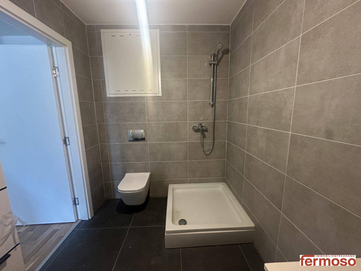 Helles Badezimmer mit Dusche und wandhängendem WC, komplett gefliest.