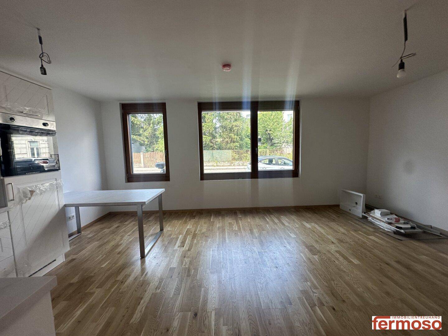 Geräumiger Wohnbereich mit hellem Holzparkettboden und großen Fenstern.