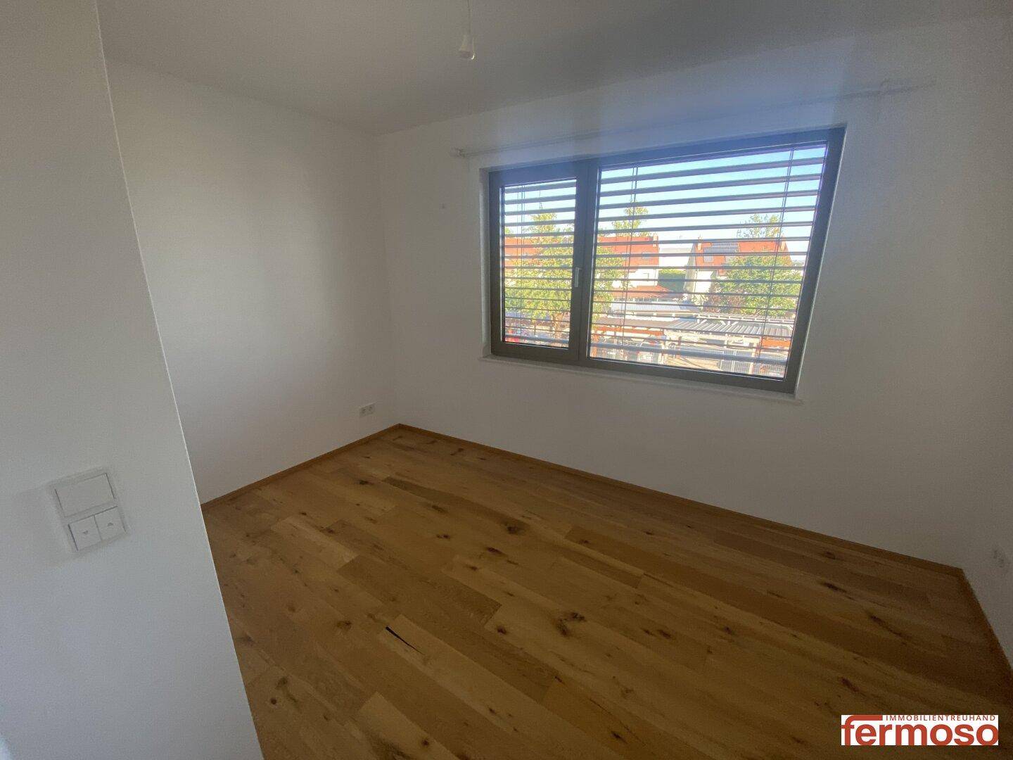 Schlafzimmer mit Holzboden und Fenster, das einen Blick ins Grüne bietet.