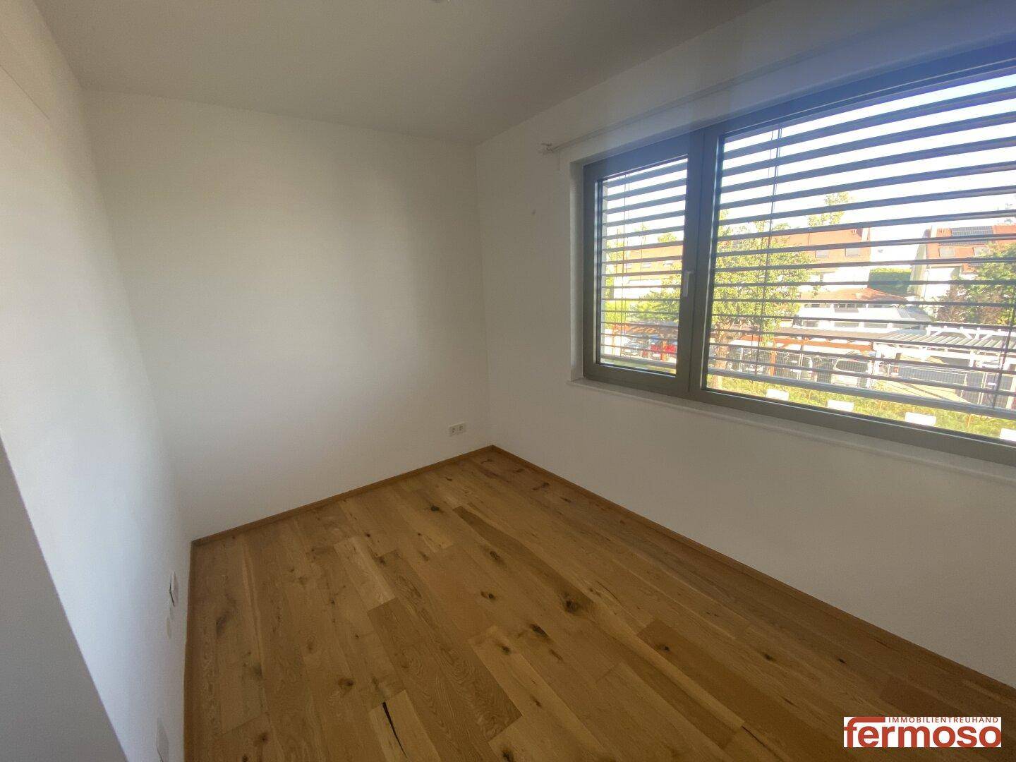 Unmöbliertes Schlafzimmer mit Holzboden und großem Fenster für viel Tageslicht.