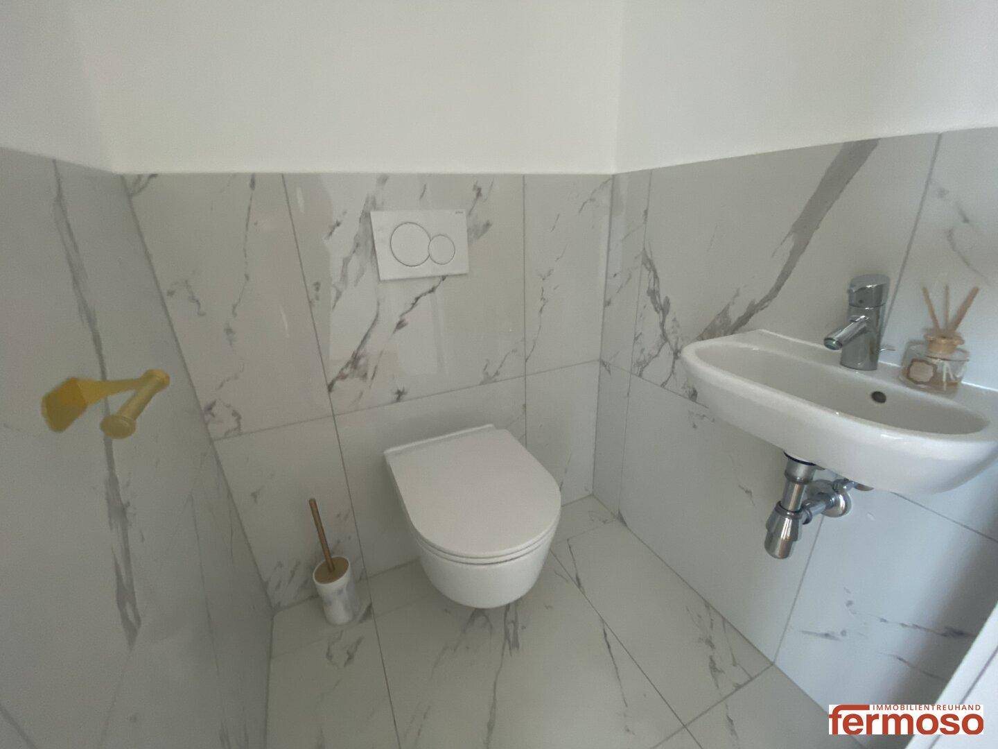 Modernes Gäste-WC mit Wand-WC, kleinem Waschbecken und Marmorfliesen.