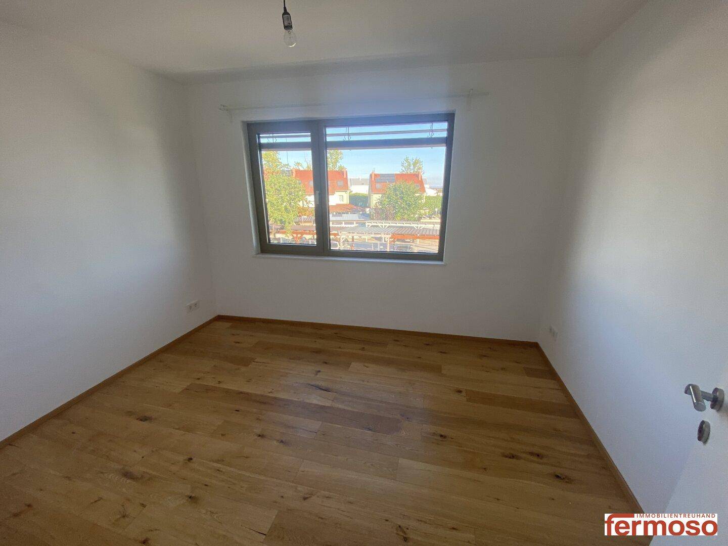 Helles Schlafzimmer mit Holzboden und Fenster, das einen Blick auf die Umgebung bietet.