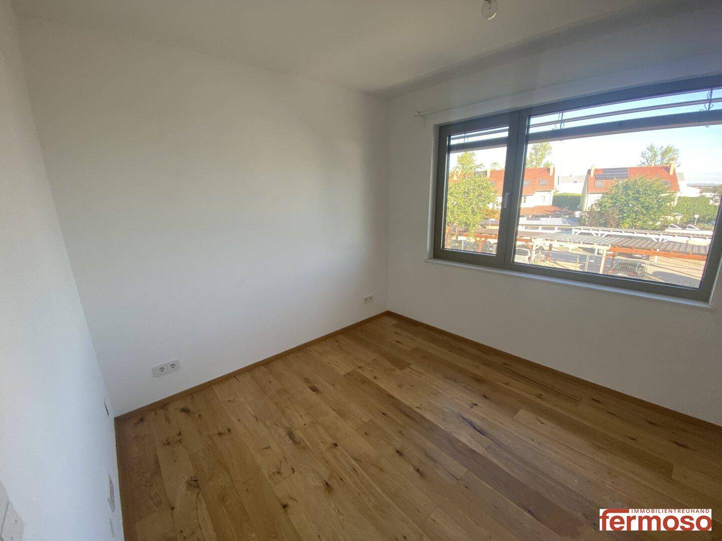 Unmöbliertes Schlafzimmer mit Holzboden und Fenster, das viel Tageslicht hereinlässt.