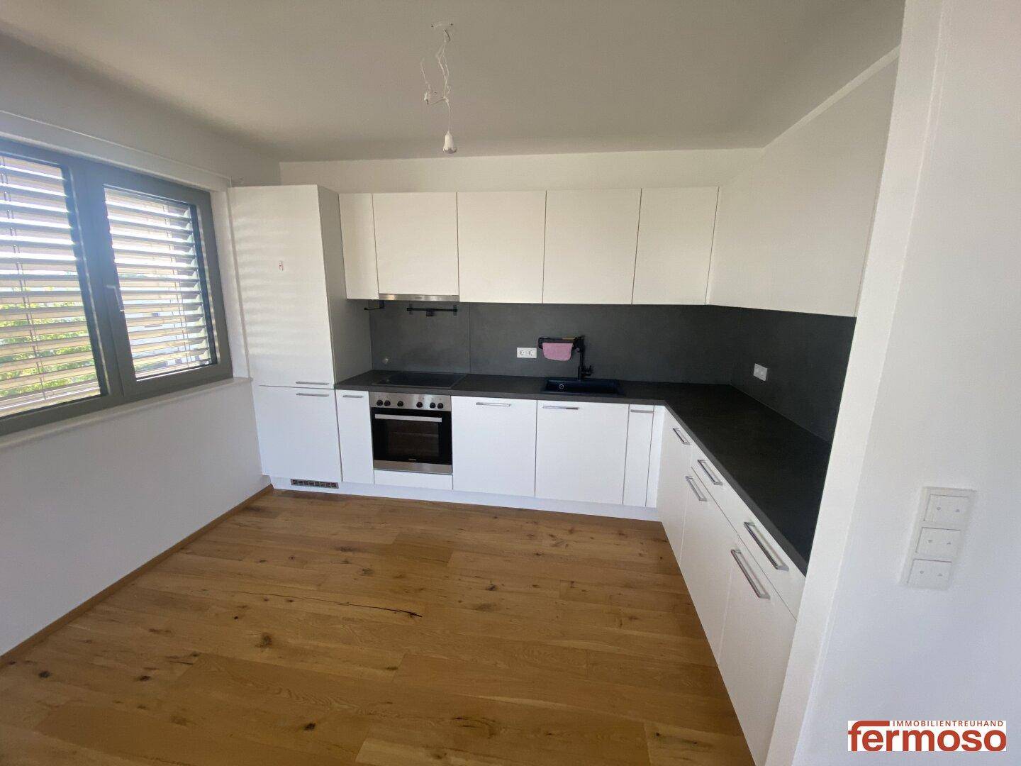 Moderne Einbauküche mit weißen Schränken, dunkler Arbeitsplatte und Holzboden.