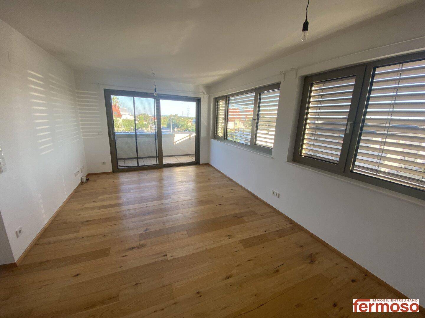 Helles, unmöbliertes Wohnzimmer mit Holzboden und Zugang zum Außenbereich.