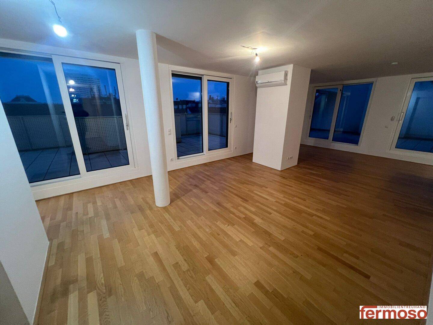 Geräumiges Wohnzimmer mit hellem Parkettboden, großen Fenstern und Zugang zur Terrasse.