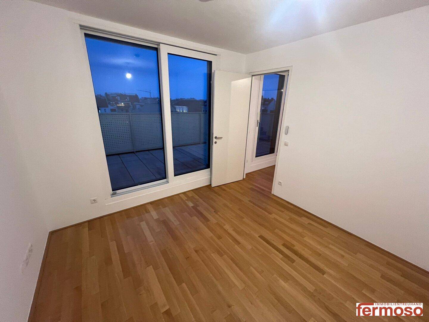 Helles Schlafzimmer mit Parkettboden und Zugang zu einem Außenbereich.