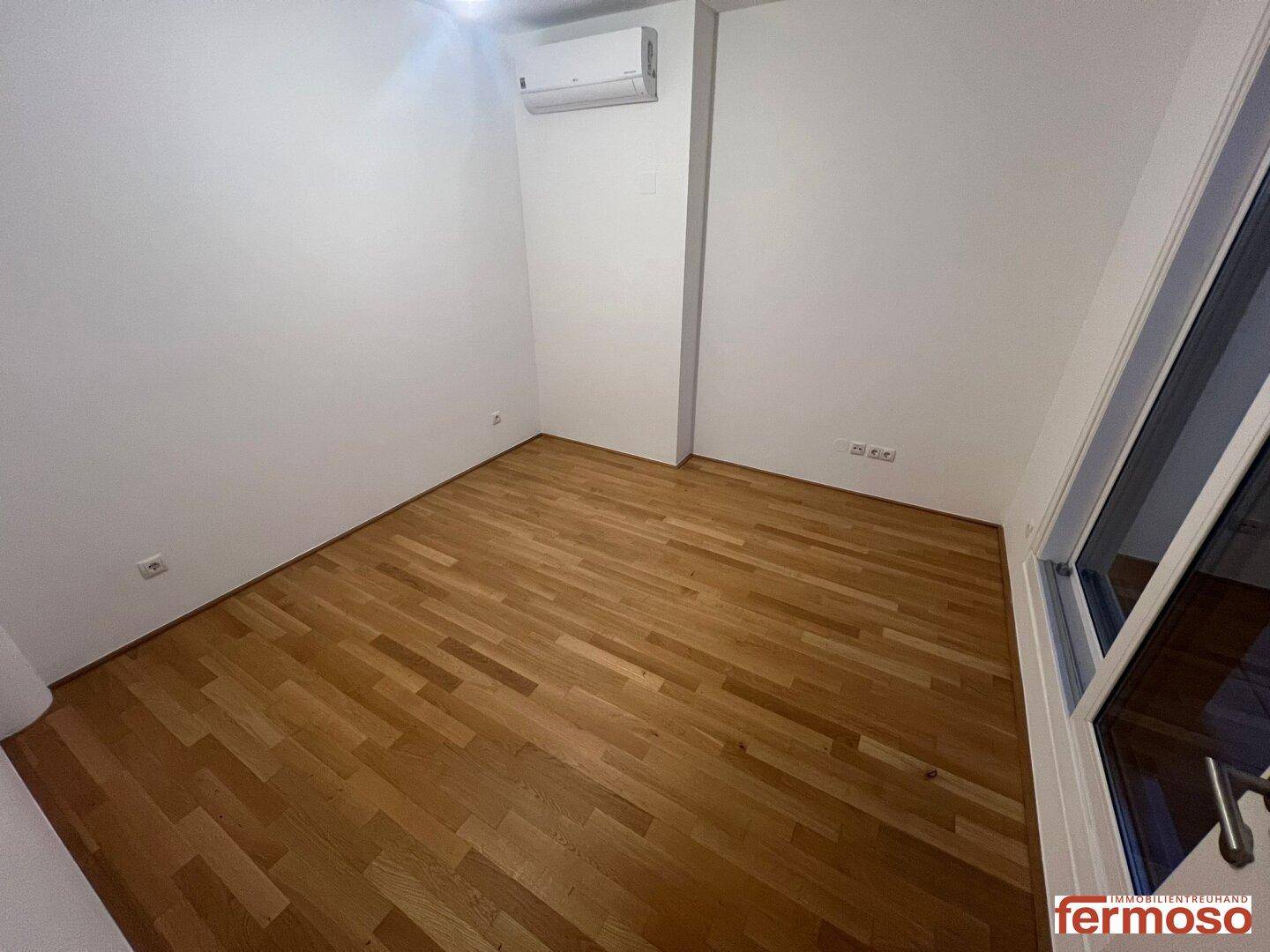 Schlafzimmer mit Parkettboden, Klimaanlage und großen Fenstern für viel Tageslicht.