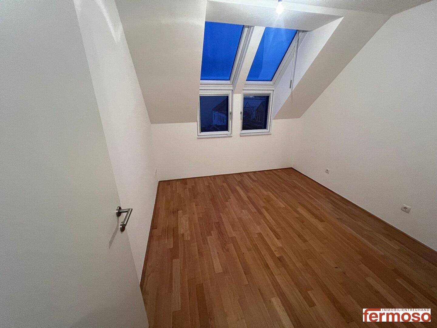 Dachgeschosszimmer mit schrägen Wänden, Parkettboden und zwei Dachfenstern für viel Licht.