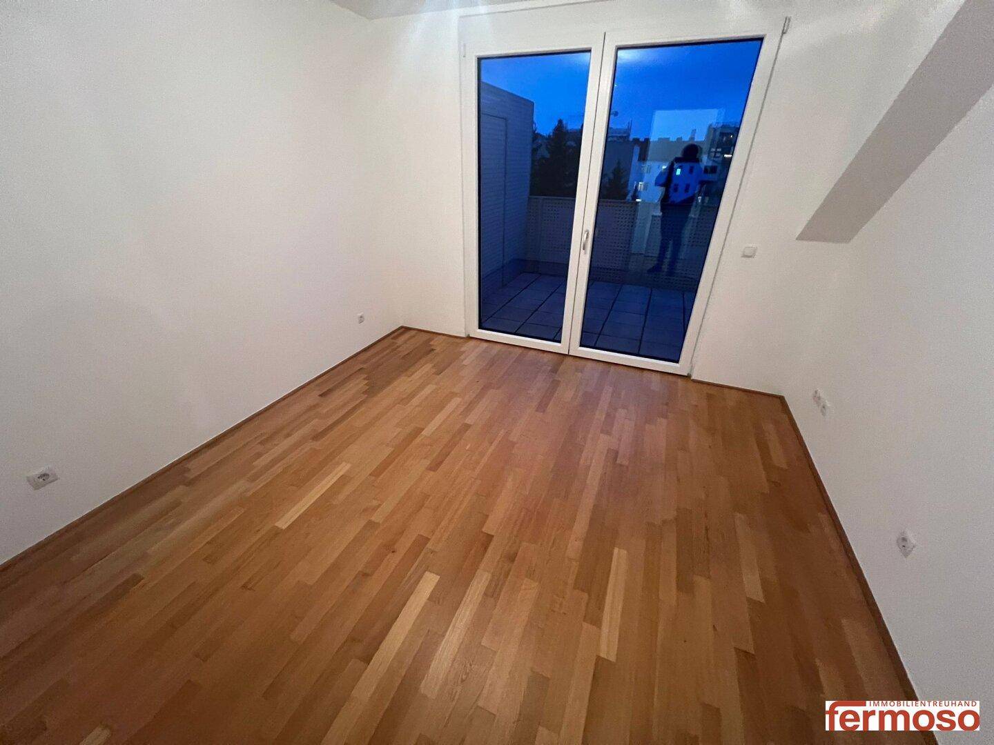 Schlafzimmer mit Parkettboden und direktem Zugang zu einem Balkon oder einer Terrasse.