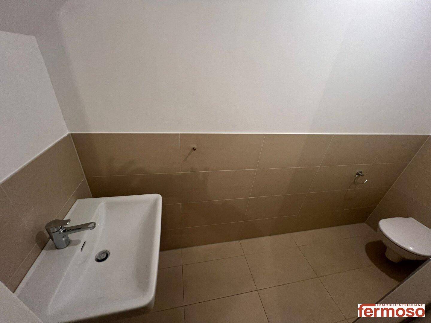 Modernes Gäste-WC mit beigefarbenen Fliesen, Waschbecken und wandhängender Toilette.