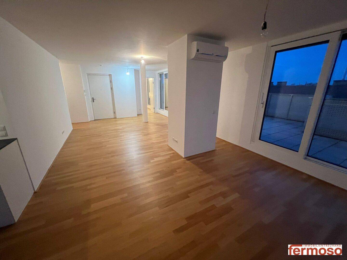 Weitläufiger Wohnbereich mit Parkettboden, Klimaanlage und großen Fenstern zur Terrasse.