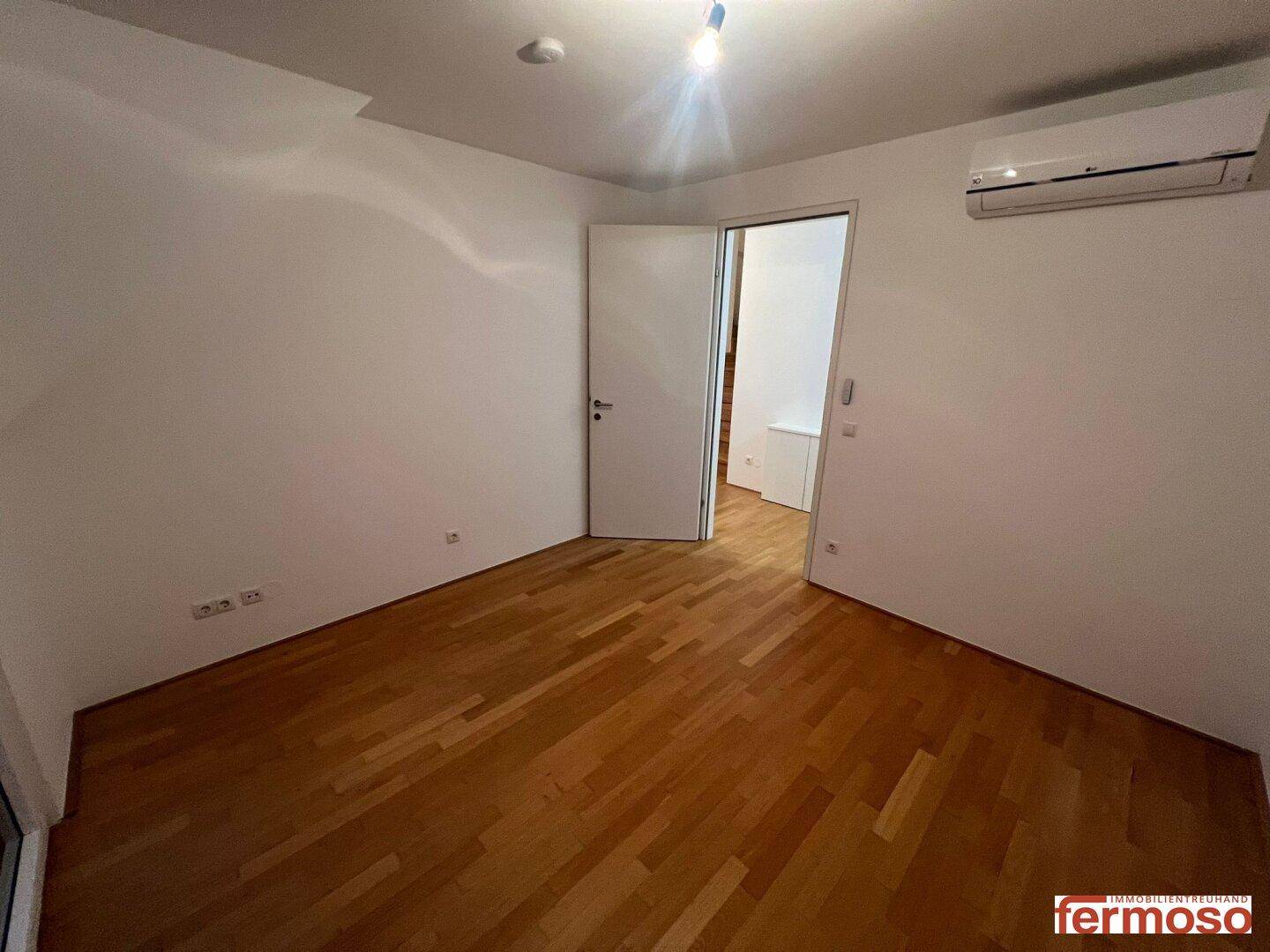 Geräumiges Schlafzimmer mit Parkettboden und installierter Klimaanlage für angenehmes Raumklima.