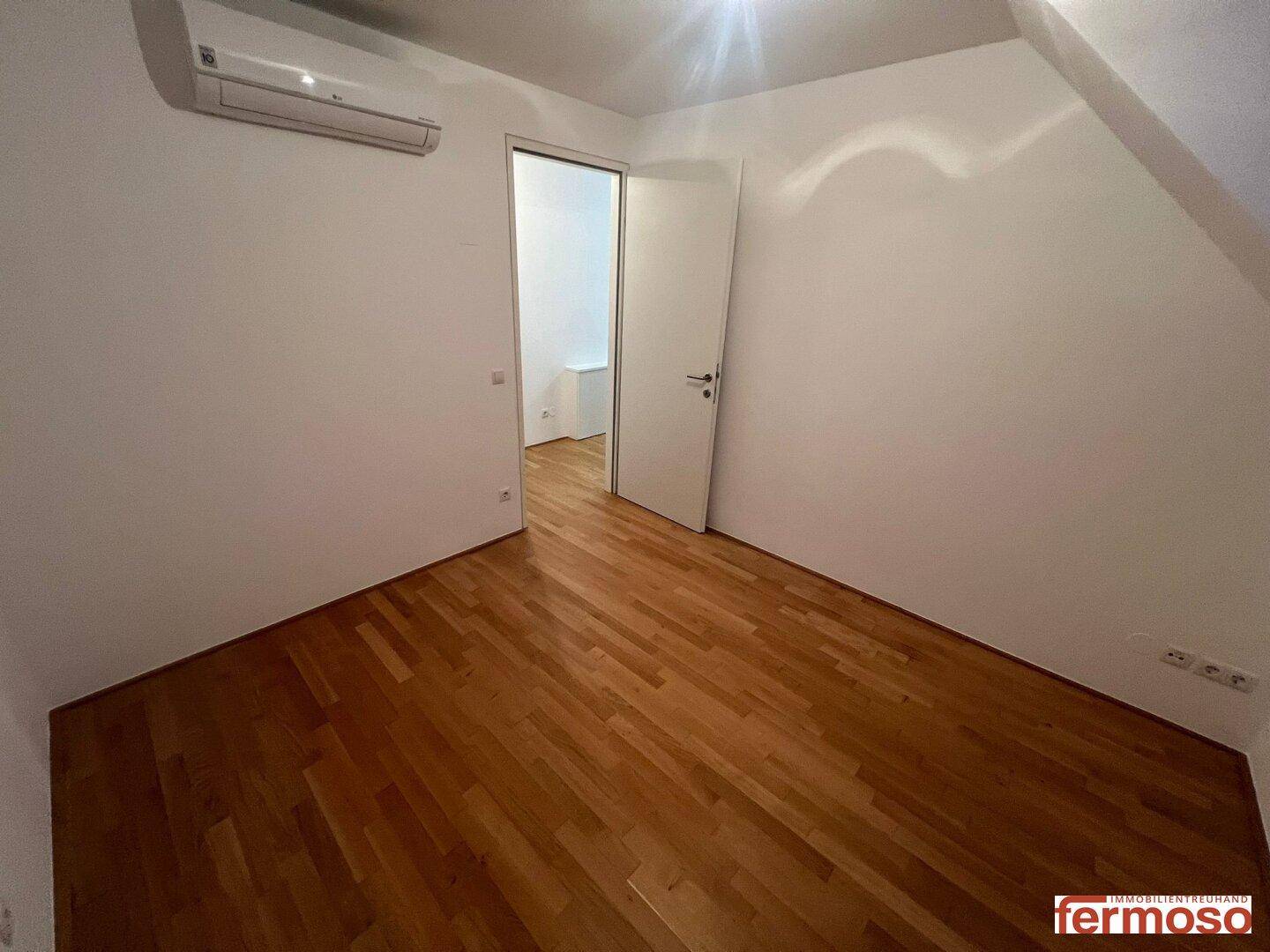 Schlafzimmer mit Parkettboden, Klimaanlage und Zugang zu einem weiteren Raum.