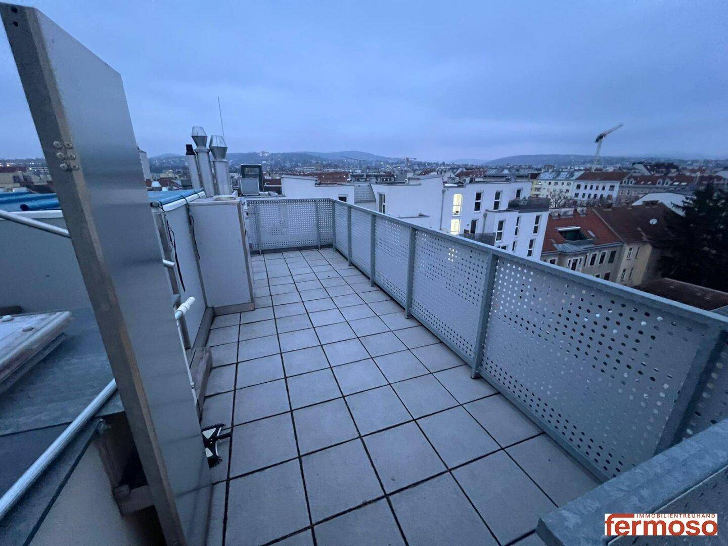 Geräumige Dachterrasse mit Fliesenboden und Panoramablick über die Dächer der Stadt.