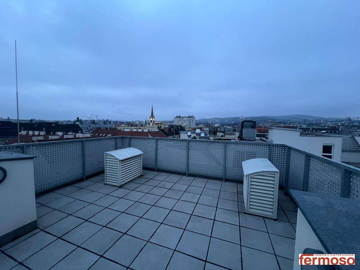 Weitläufige Dachterrasse mit Stadtblick und Lüftungsanlagen auf dem Dach.
