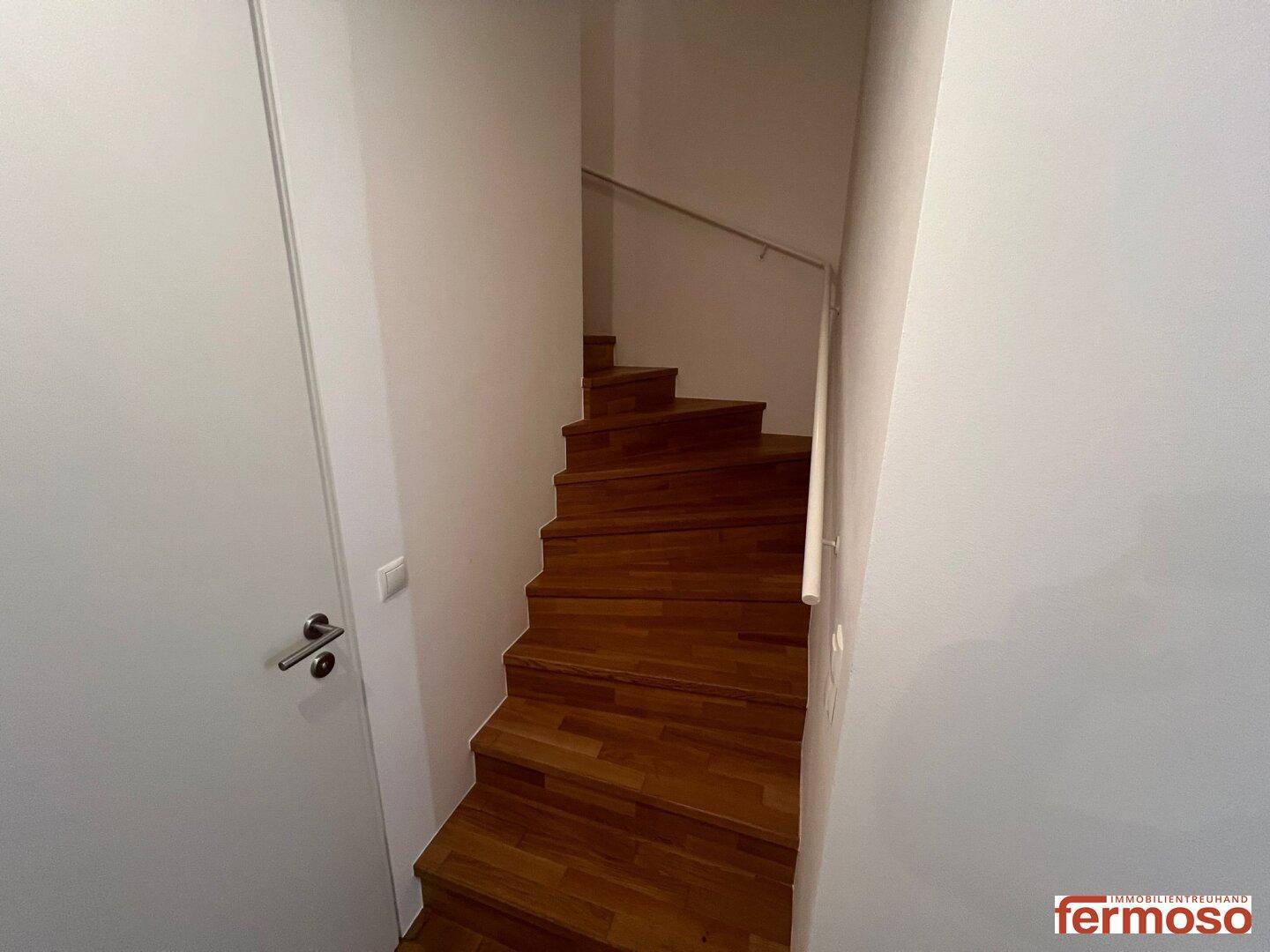 Wendeltreppe aus Holz mit schlichtem Geländer, die in die obere Etage führt.