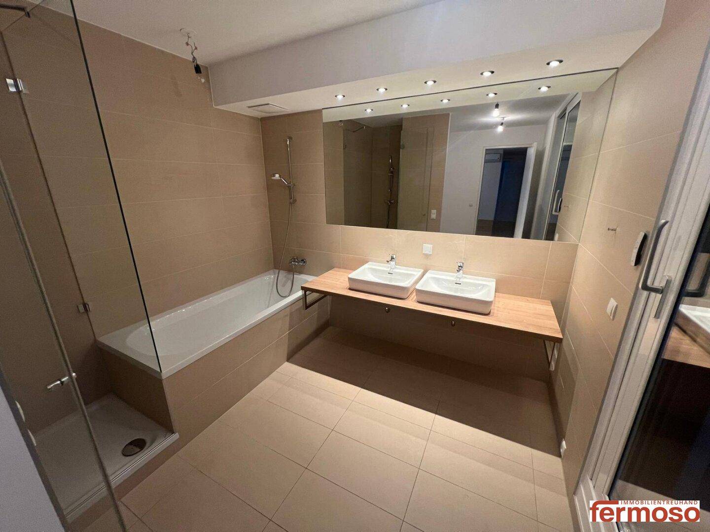 Modernes Badezimmer mit Doppelwaschbecken, Badewanne, Dusche und großen Spiegeln.