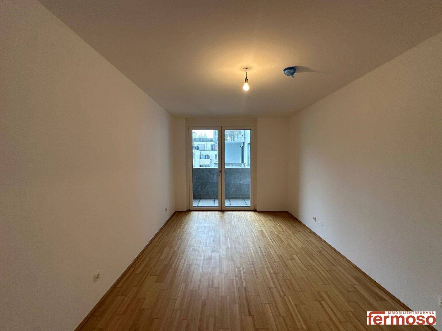 Leeres Schlafzimmer mit Parkettboden und Zugang zu einem privaten Balkon.