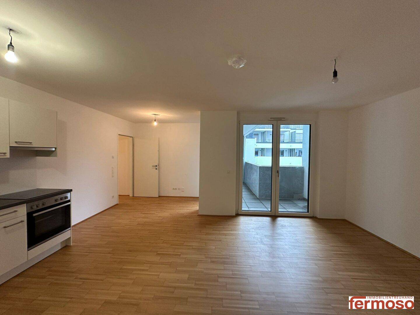 Geräumiger Wohnbereich mit Holzboden und großem Balkonzugang, der viel Licht hereinlässt.