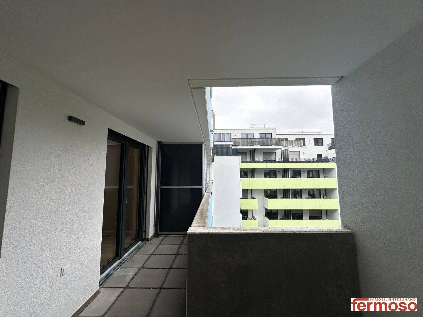 Langer Balkon mit Fliesenboden und Ausblick auf den Innenhof und die Nachbarschaft.