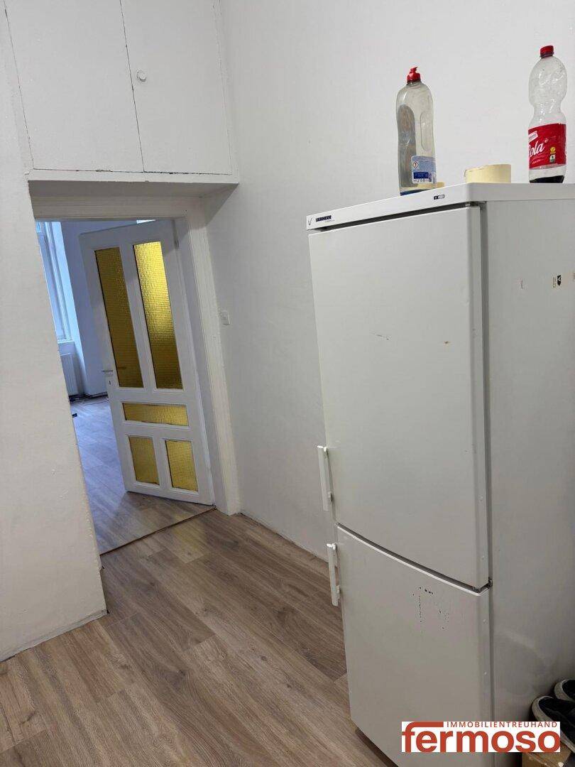 Eine kleine Küchenzeile mit Kühlschrank und Zugang zu einem weiteren Raum mit Laminatboden, ideal für Singles.