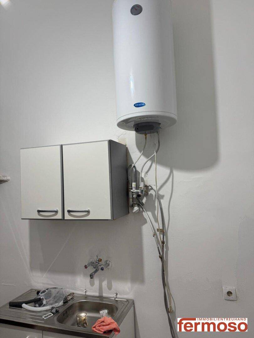 Ein Waschbecken mit Unterschrank und ein Warmwasserboiler an einer weißen Wand, praktisch für den Hauswirtschaftsraum.