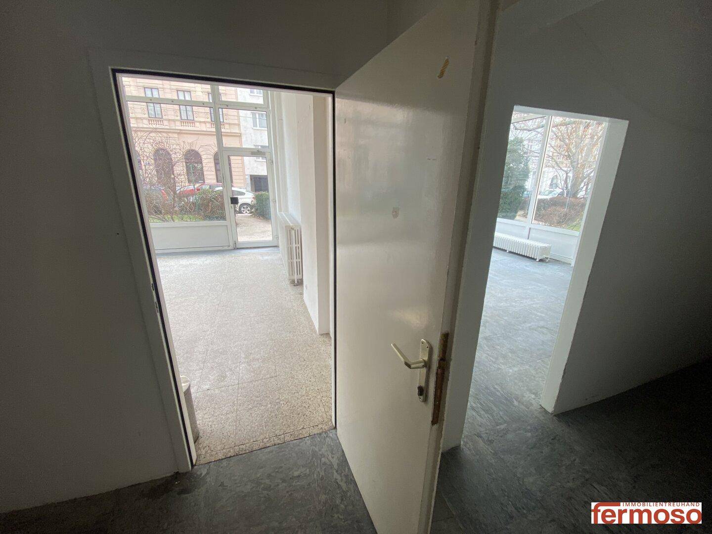 Blick durch eine offene Tür in zwei angrenzende Räume mit unterschiedlichen Bodenbelägen.