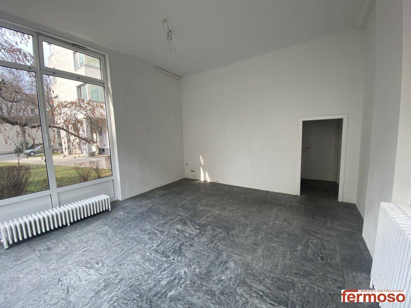 Leerer Raum mit dunklem Bodenbelag und großen Fenstern, bietet viel Tageslicht.