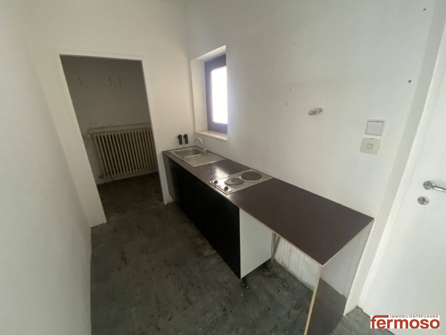 Kompakte Küchenzeile mit Spüle und Kochplatten, beleuchtet durch ein kleines Fenster.