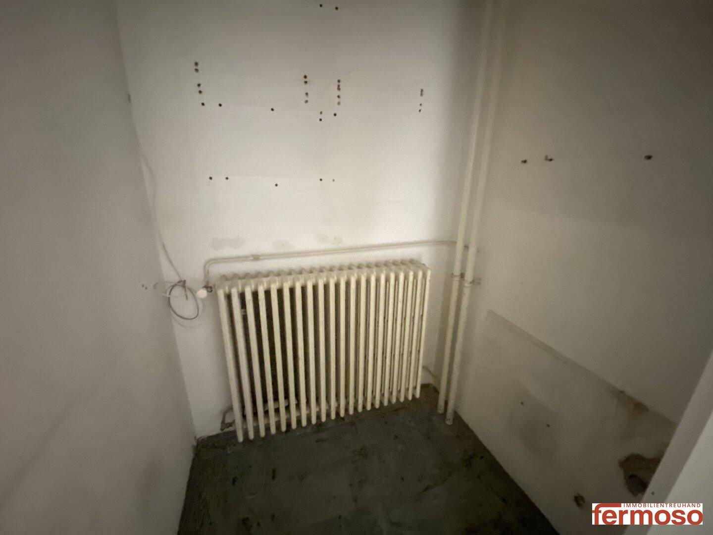 Kleiner Abstellraum oder Technikraum mit Heizkörper und weißen Wänden.