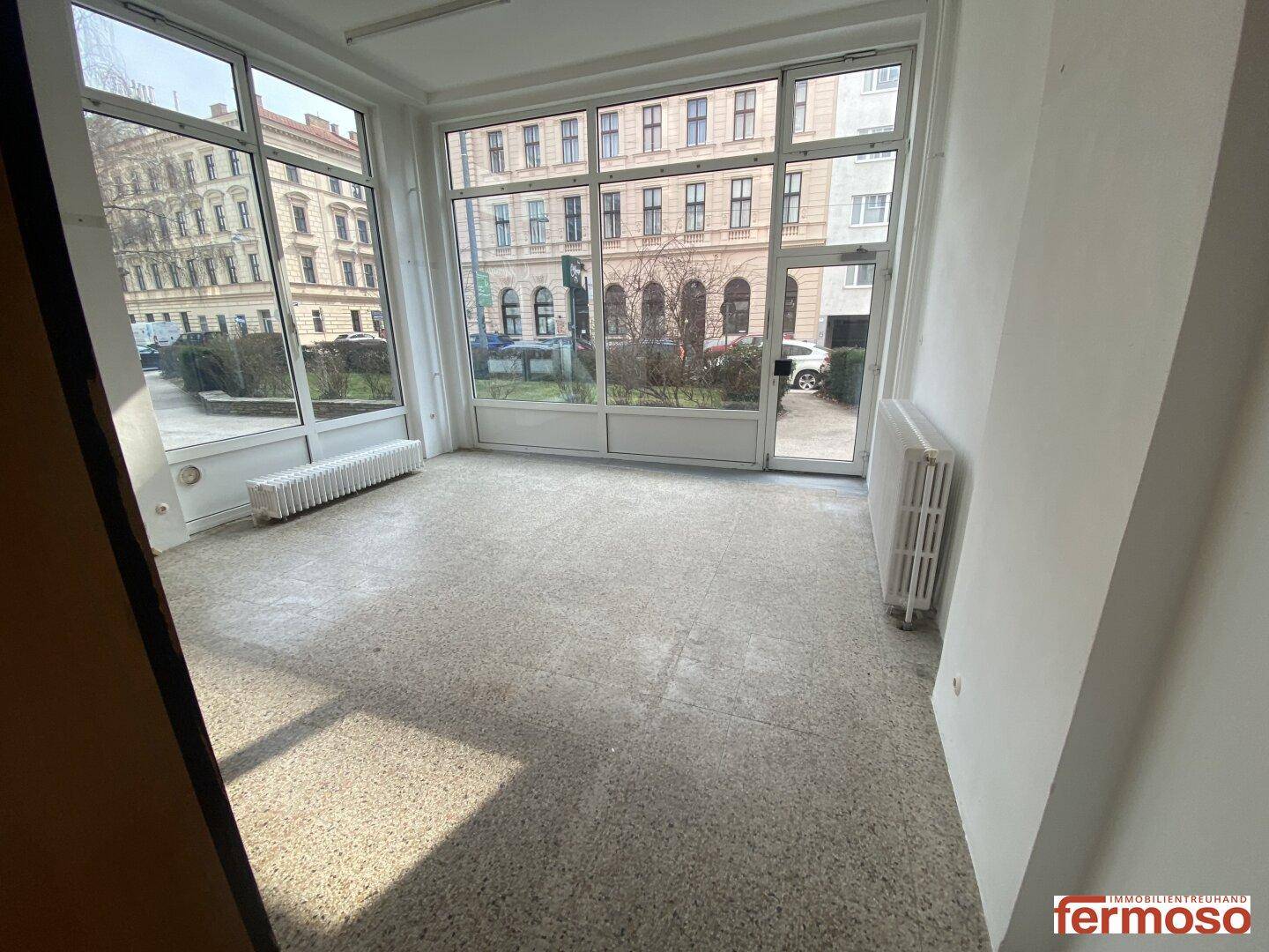 Heller, leerer Geschäftsraum mit großen Fenstern und Terrazzoboden, vielseitig nutzbar.