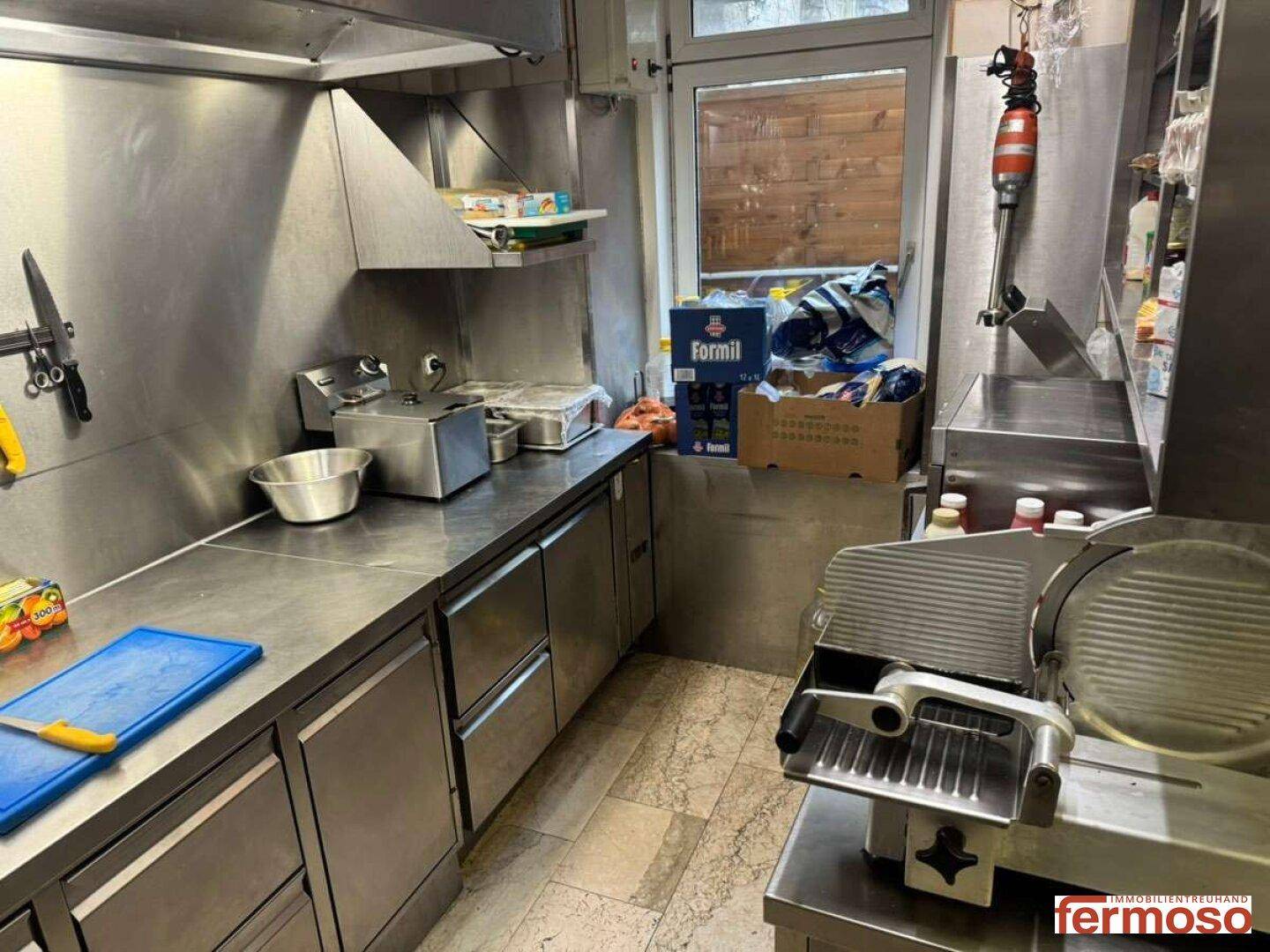 Funktionale Gewerbeküche mit Edelstahlmöbeln, Arbeitsflächen und einem Fenster mit Blick nach draußen.